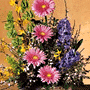 basket arrangement of brightly colored pink, purple and yellow flowers and dark leafy greens in a whitewash wicker basket.